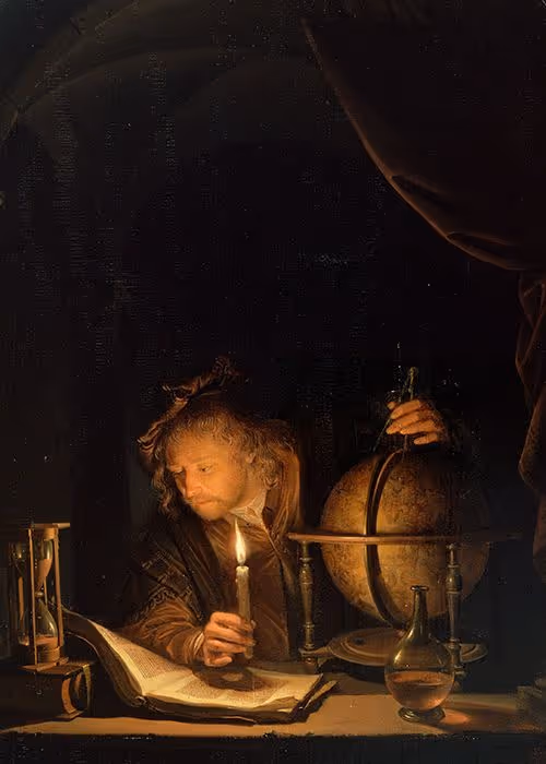 A scholar illuminated by candlelight studying an open book beside a globe, hourglass, and glass flask in a dark room.